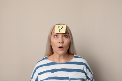 Emotional mature woman with question mark on beige background