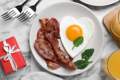 Photo of Romantic breakfast with fried bacon and heart shaped egg on white marble table, flat lay. Valentine's day celebration