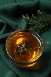 Glass cup of aromatic herbal tea with thyme on green fabric