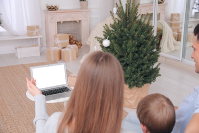 Photo of Family with child using video chat on laptop in room decorated for Christmas, back view