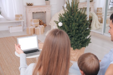 Family with child using video chat on laptop in room decorated for Christmas, back view