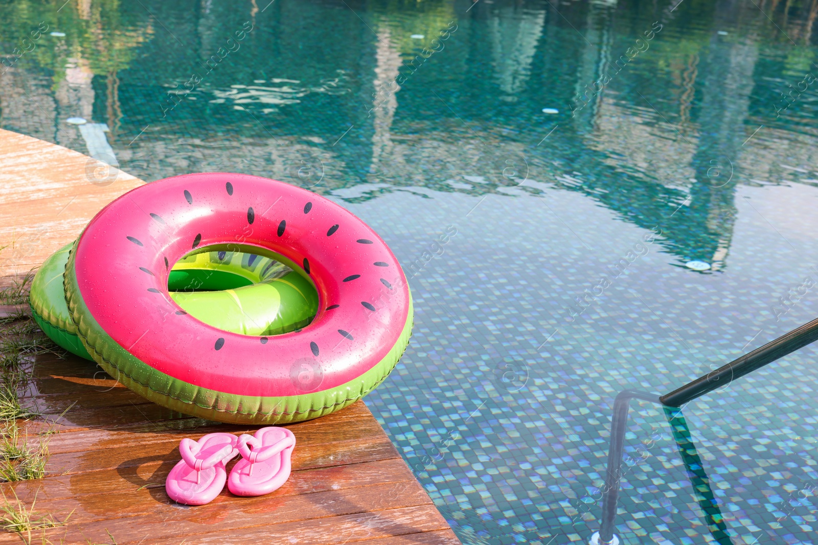 Photo of Inflatable rings and flip flops on wooden deck near swimming pool. Luxury resort