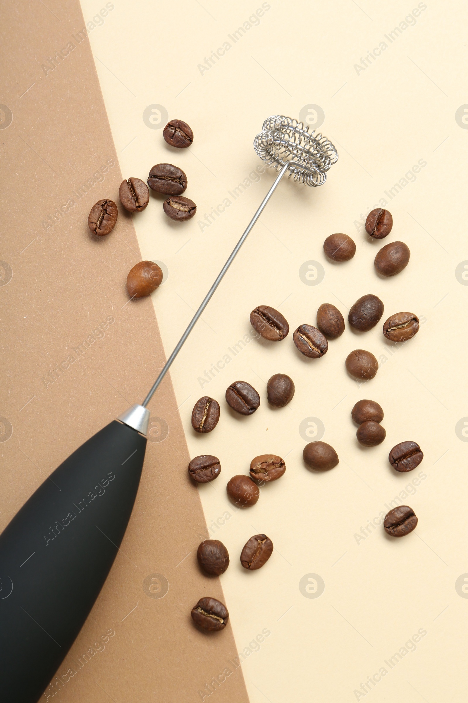 Photo of Milk frother wand and coffee beans on color background, top view