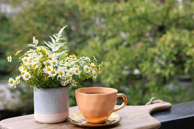 Cup of delicious chamomile tea and fresh flowers outdoors. Space for text