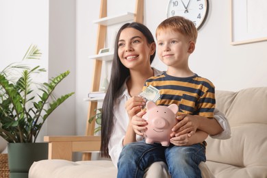 Photo of Mother with money and her son holding piggy bank at home, space for text