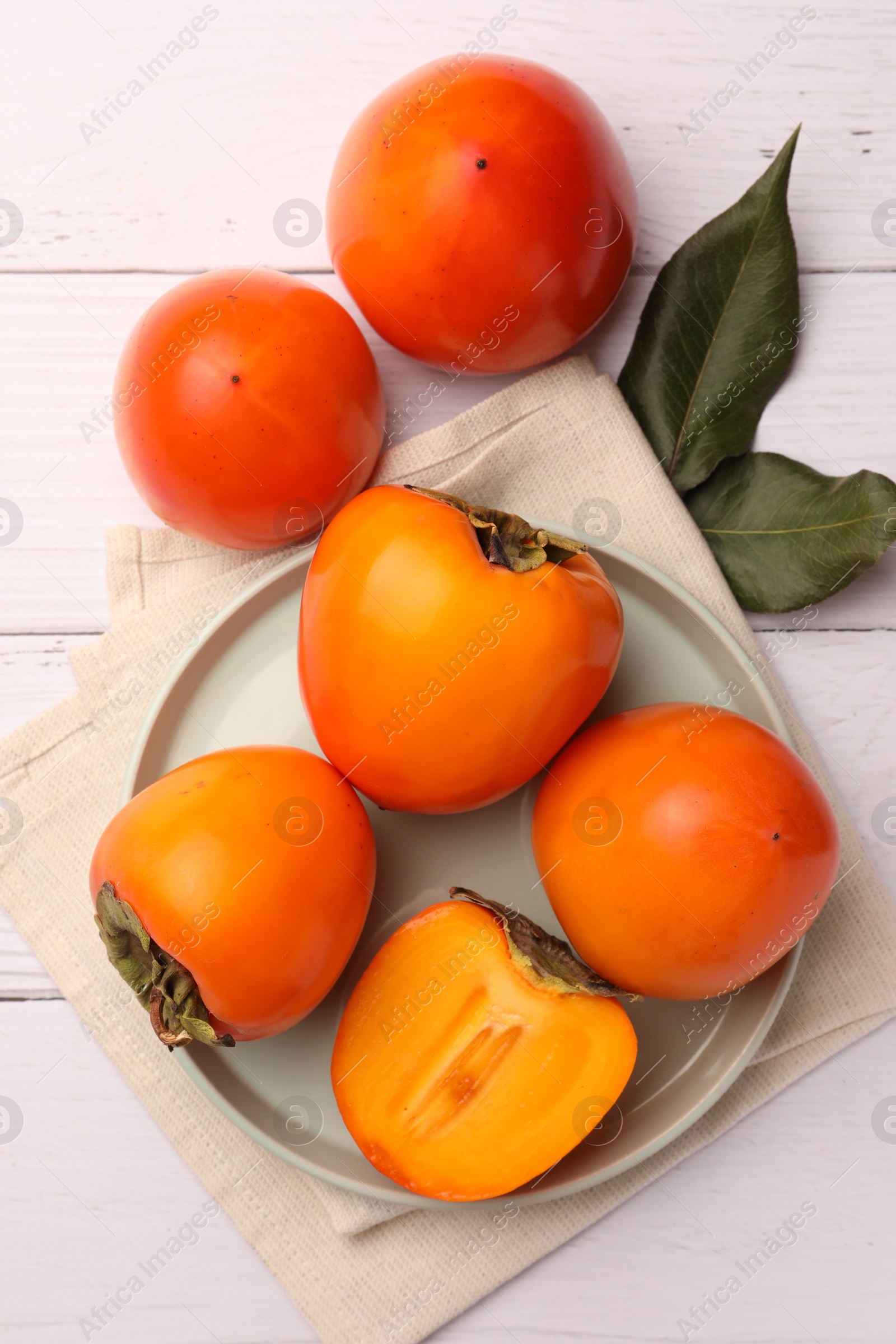 Photo of Delicious ripe juicy persimmons on white wooden table, flat lay