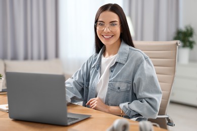 Photo of Young woman watching webinar at table in room