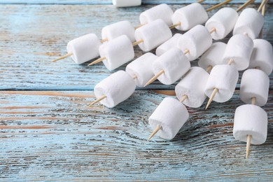 Photo of Sticks with delicious puffy marshmallows on light blue wooden table. Space for text