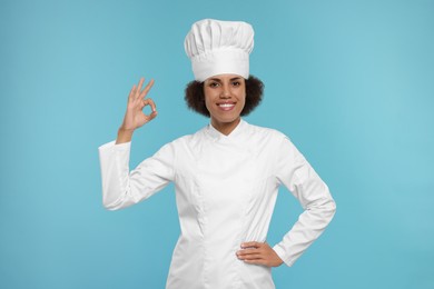 Photo of Happy female chef in uniform showing ok gesture on light blue background