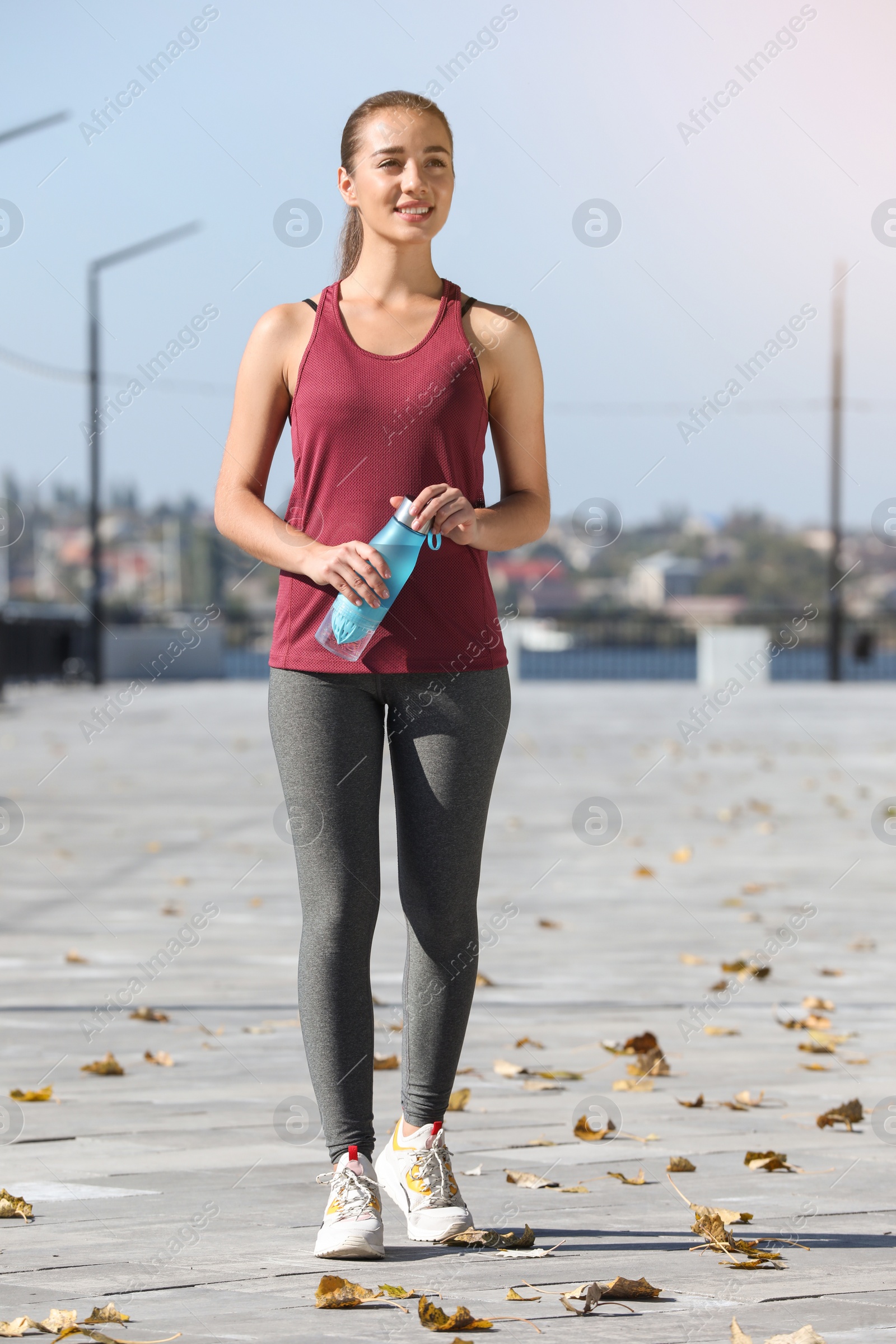 Photo of Young sporty woman holding bottle of water outdoors on sunny day