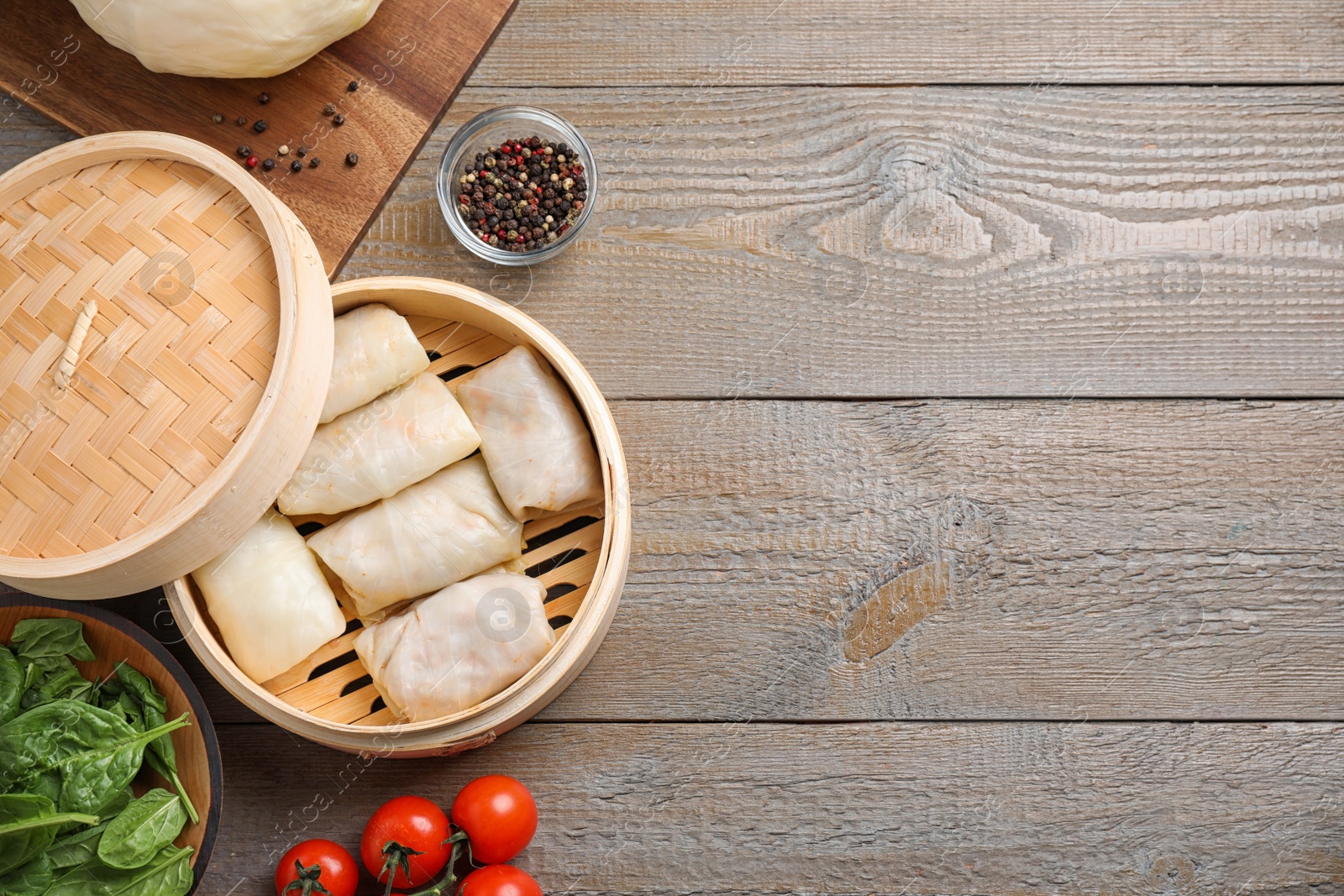 Photo of Delicious cabbage rolls in bamboo steamer on wooden table, flat lay. Space for text