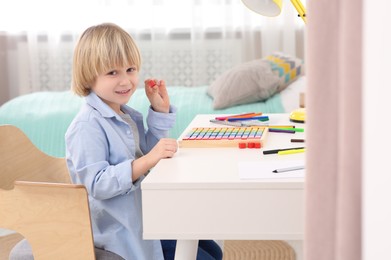 Photo of Cute little boy with colorful wooden cubes at desk in room. Home workplace