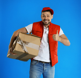 Photo of Emotional courier with damaged cardboard box on blue background. Poor quality delivery service