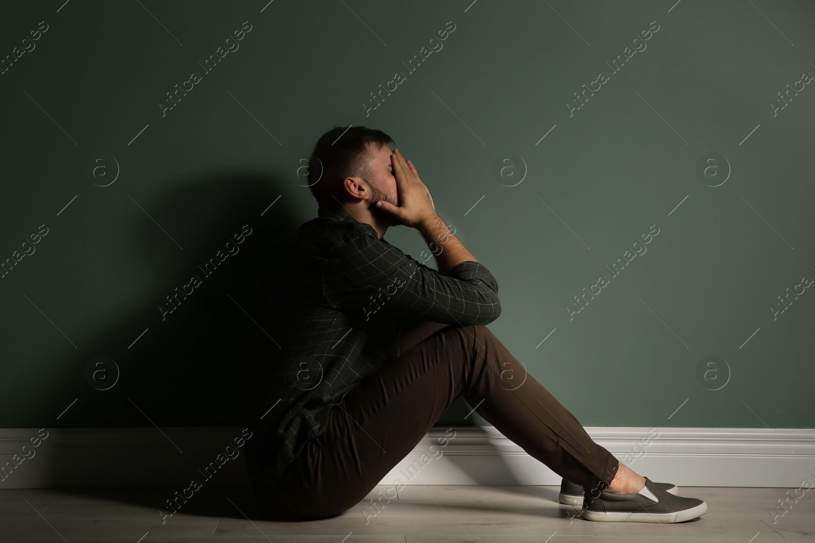 Photo of Depressed young man sitting on floor in darkness