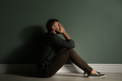 Depressed young man sitting on floor in darkness