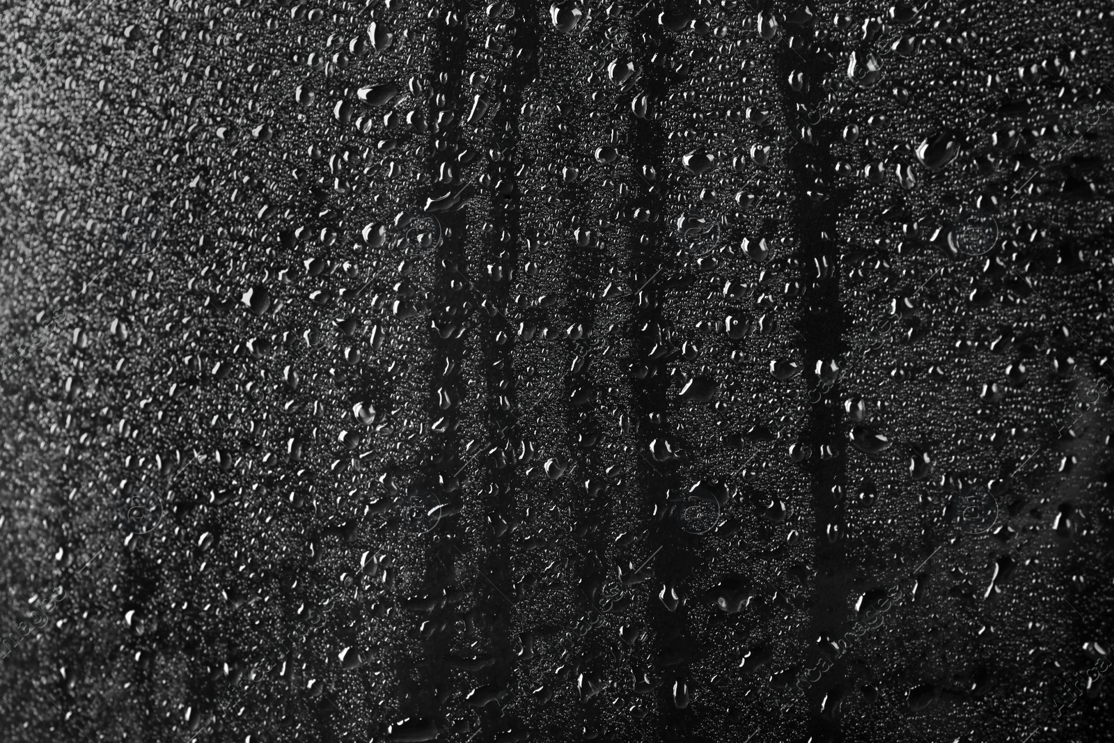 Photo of Glass with rain drops against dark background