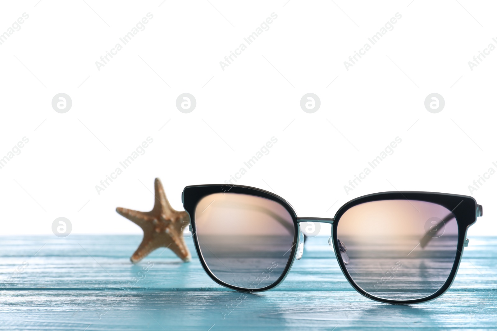 Photo of Stylish sunglasses and starfish on light blue wooden table against white background