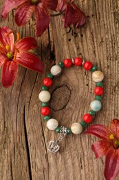 Photo of Beautiful bracelet with gemstones and lily flowers on wooden surface, flat lay
