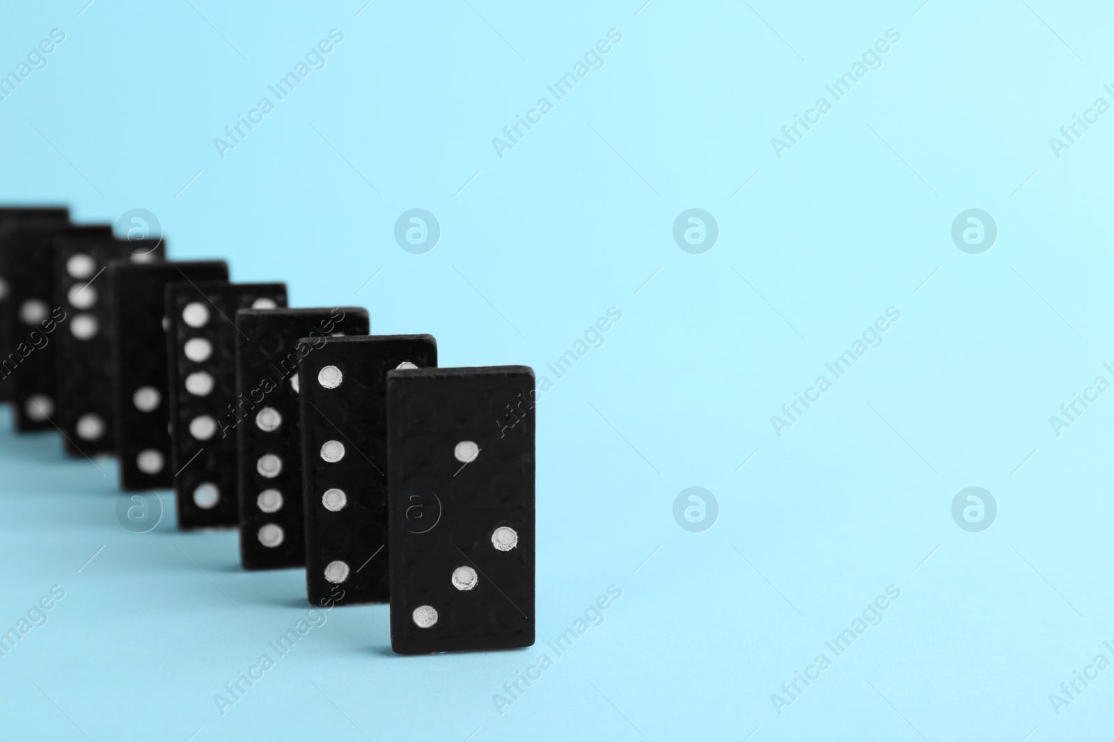 Photo of Row of black domino tiles on light blue background. Space for text