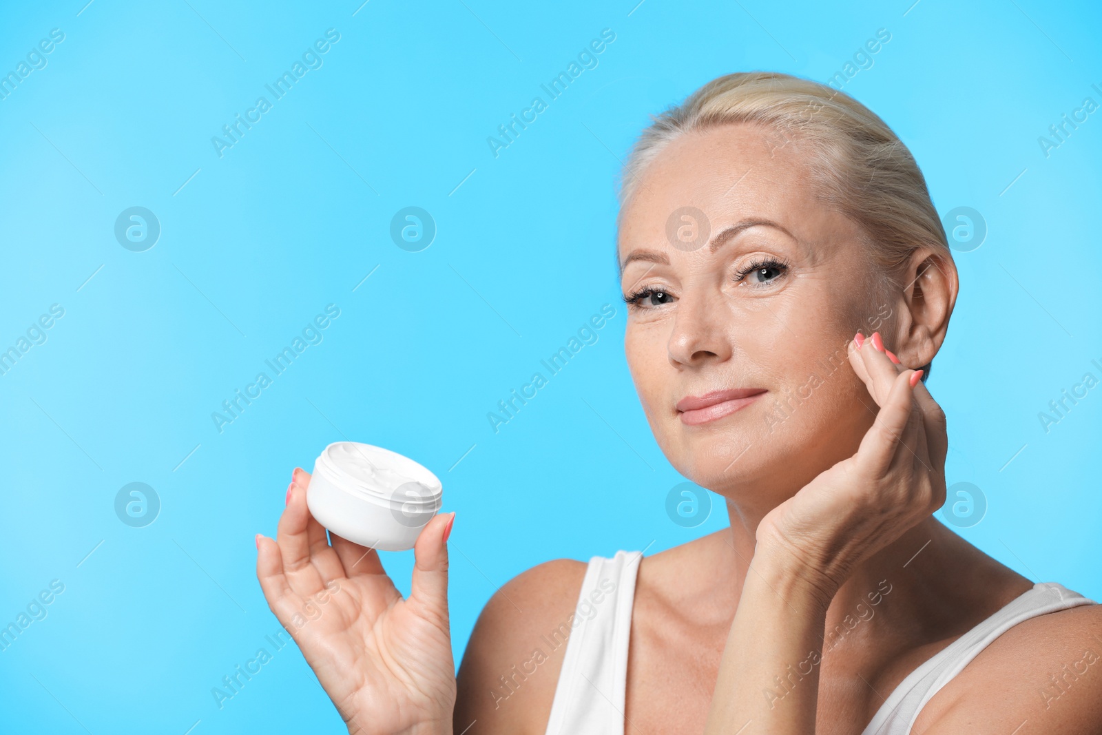 Photo of Portrait of beautiful mature woman with perfect skin holding jar of cream on light blue background