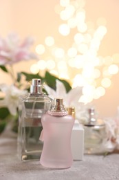 Photo of Bottles of perfume on table against beautiful lily flowers and blurred lights, closeup. Space for text