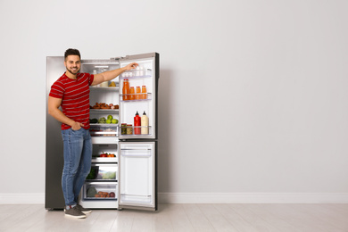 Photo of Young man taking yoghurt out of refrigerator indoors, space for text