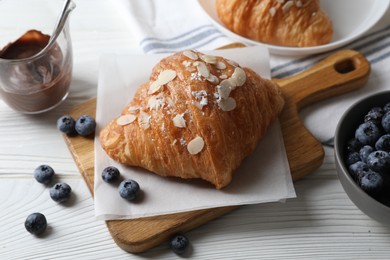 Delicious croissants with almond flakes and blueberries on white wooden table, closeup