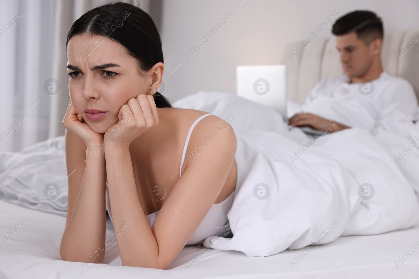 Photo of Internet addiction. Man with laptop ignoring his girlfriend in bedroom