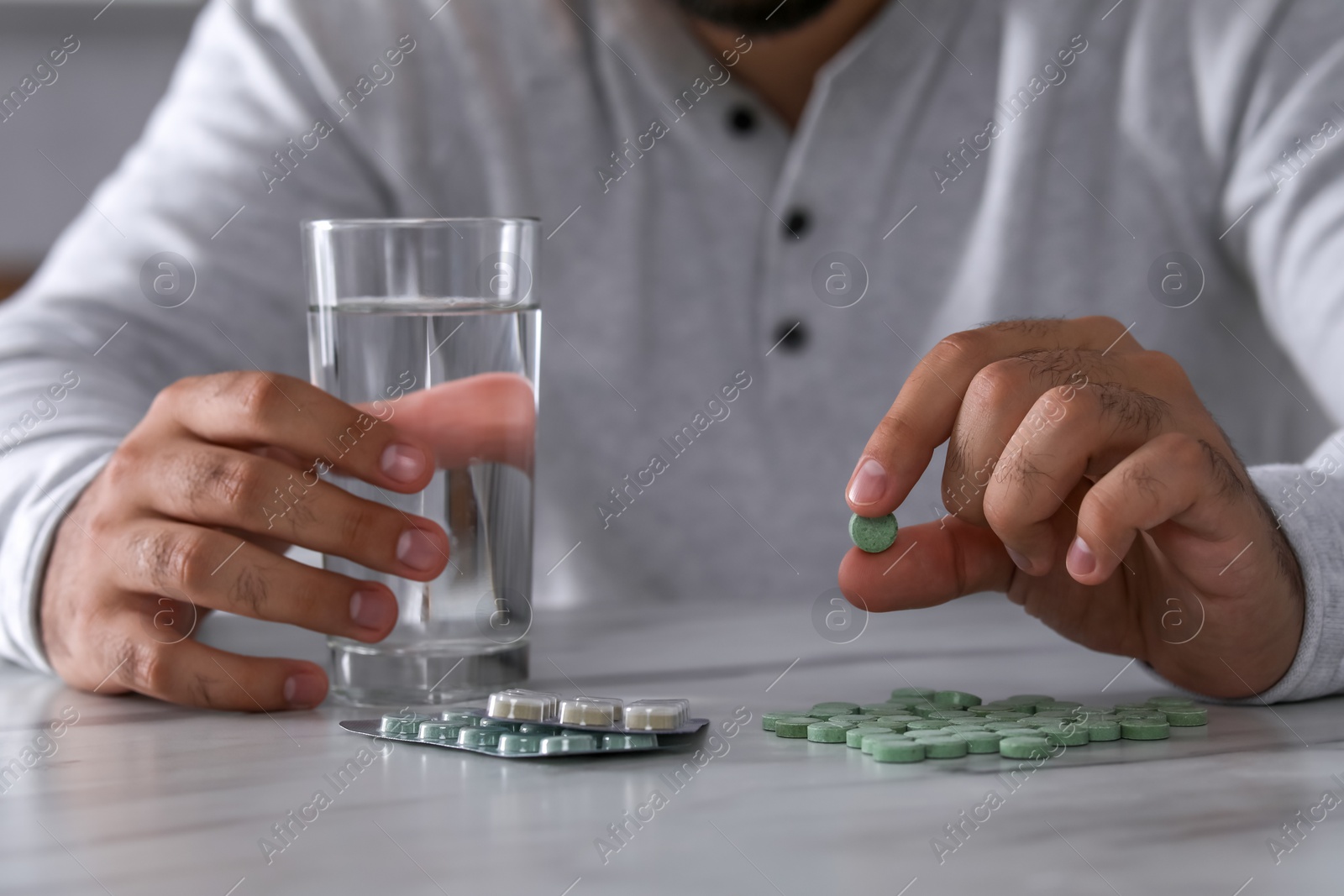 Photo of Man holding antidepressant pill and glass of water at white marble table, closeup