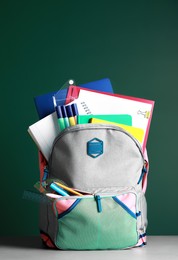 Backpack with different school stationery on white table near chalkboard