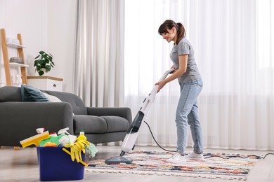 Happy young housewife vacuuming rug at home