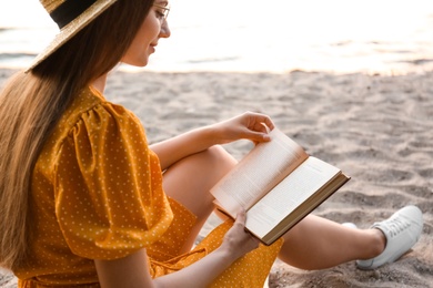 Young woman reading book on sandy beach