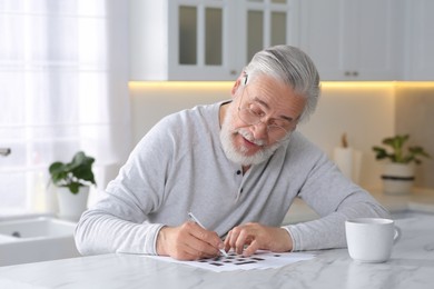 Senior man solving crossword at table in kitchen