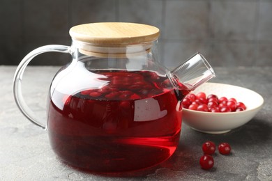 Photo of Tasty hot cranberry tea in teapot and fresh berries on light grey textured table