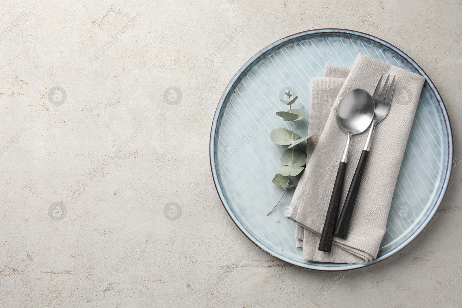 Photo of Stylish setting with cutlery, napkin, eucalyptus branch and plate on light grey table, top view. Space for text