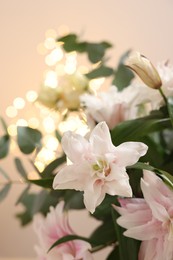 Bouquet of beautiful lily flowers against beige background with blurred lights, closeup