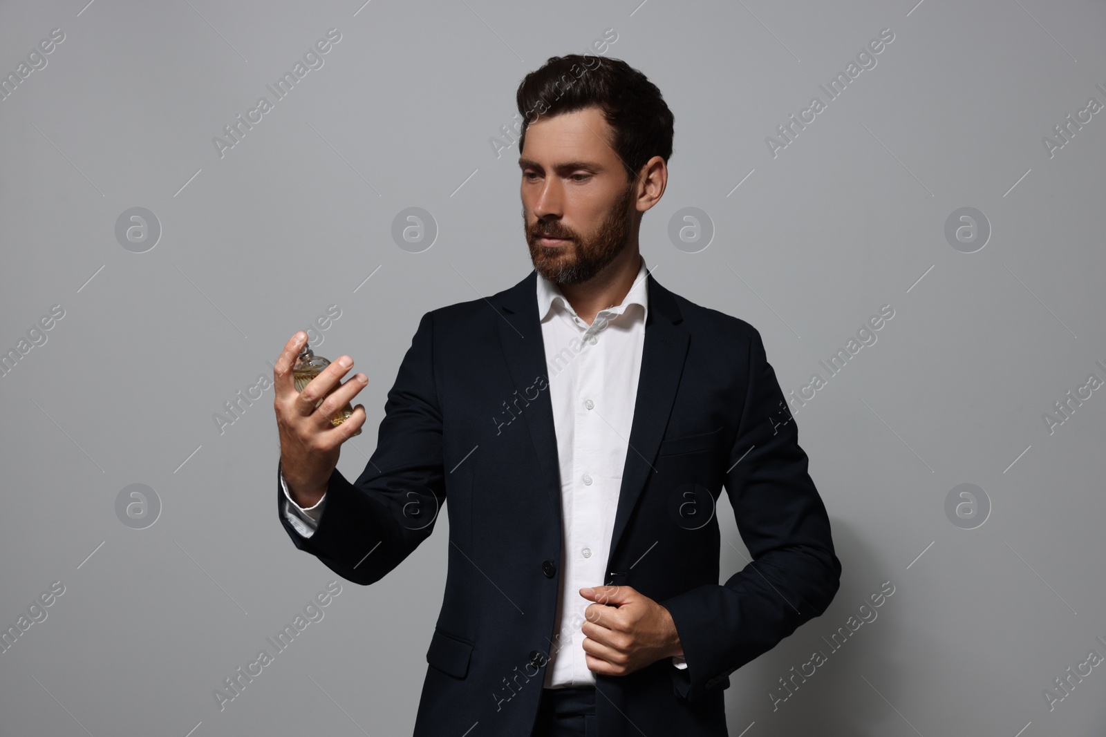 Photo of Handsome bearded man with bottle of perfume on light grey background