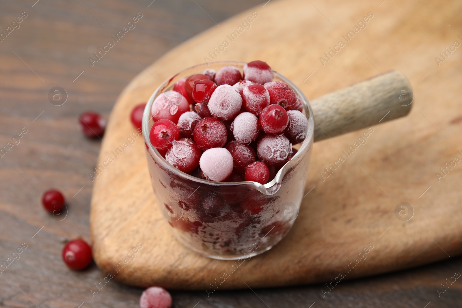 Photo of Frozen red cranberries in glass pot on wooden table, closeup