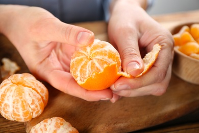 Woman peeling fresh ripe tangerine at wooden table, closeup