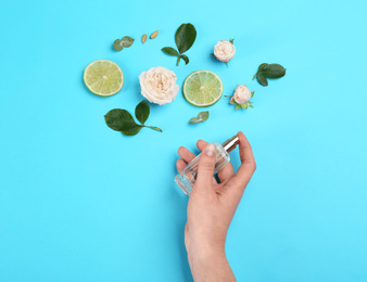 Top view of woman spraying perfume on blue background, flowers and lime representing aroma