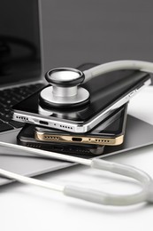Stack of electronic devices and stethoscope on white table