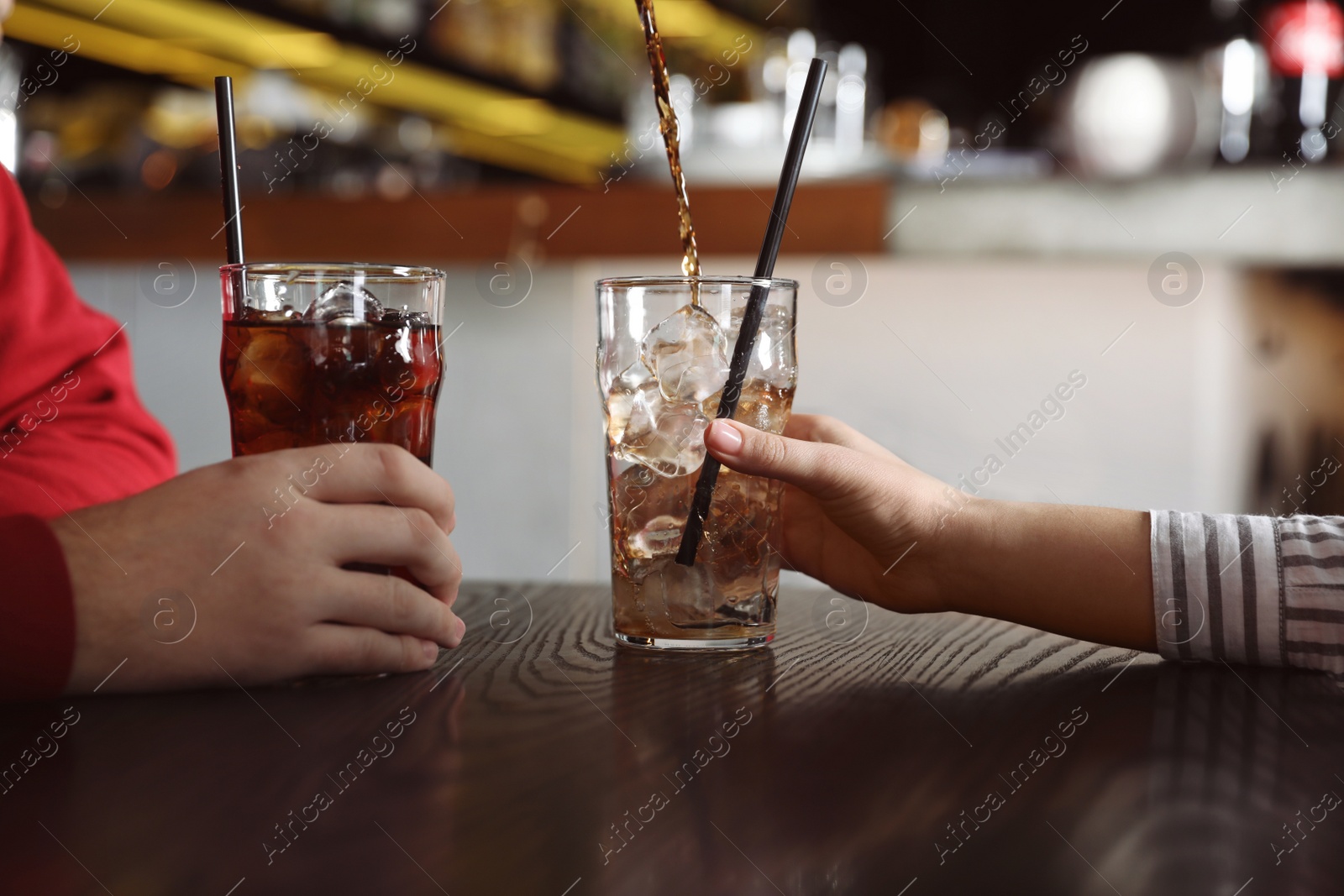 Photo of Couple with glasses of  cola at table indoors, closeup. Pouring refreshing beverage