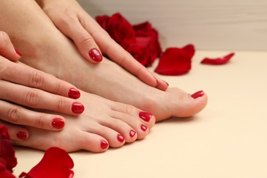Photo of Woman with stylish red toenails after pedicure procedure and rose petals on beige background, closeup