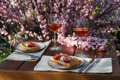 Photo of Delicious Belgian waffles with fresh strawberries and wine served on table in garden