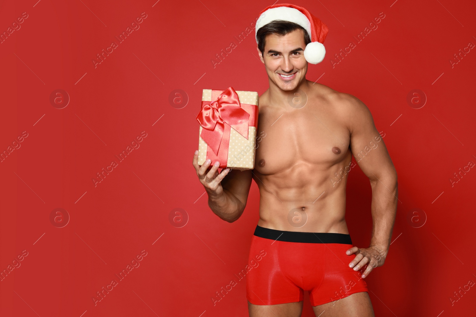 Photo of Sexy shirtless Santa Claus with gift on red background, space for text