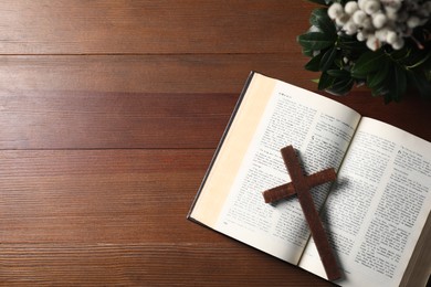 Photo of Bible, plant with willow branches and cross on wooden table, flat lay. Space for text