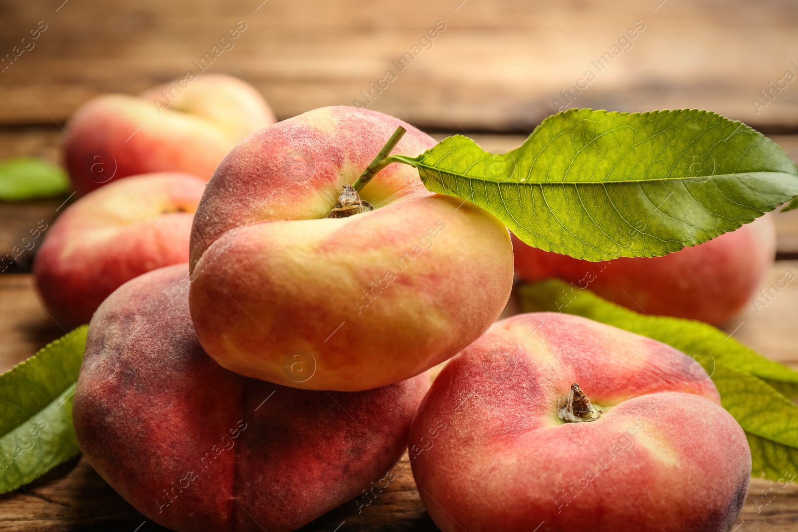 Photo of Fresh ripe donut peaches with leaves on wooden table, closeup