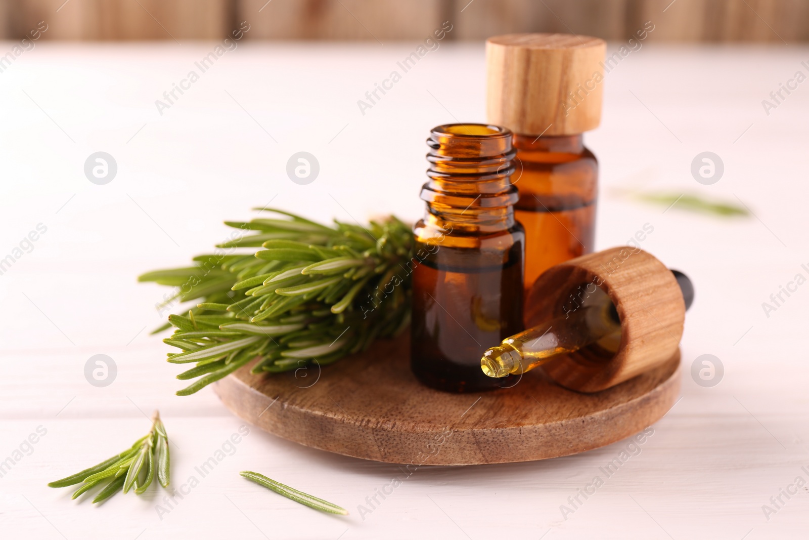 Photo of Essential oil in bottles, dropper and rosemary on white wooden table