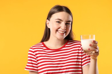 Photo of Happy woman with milk mustache holding glass of tasty dairy drink on orange background