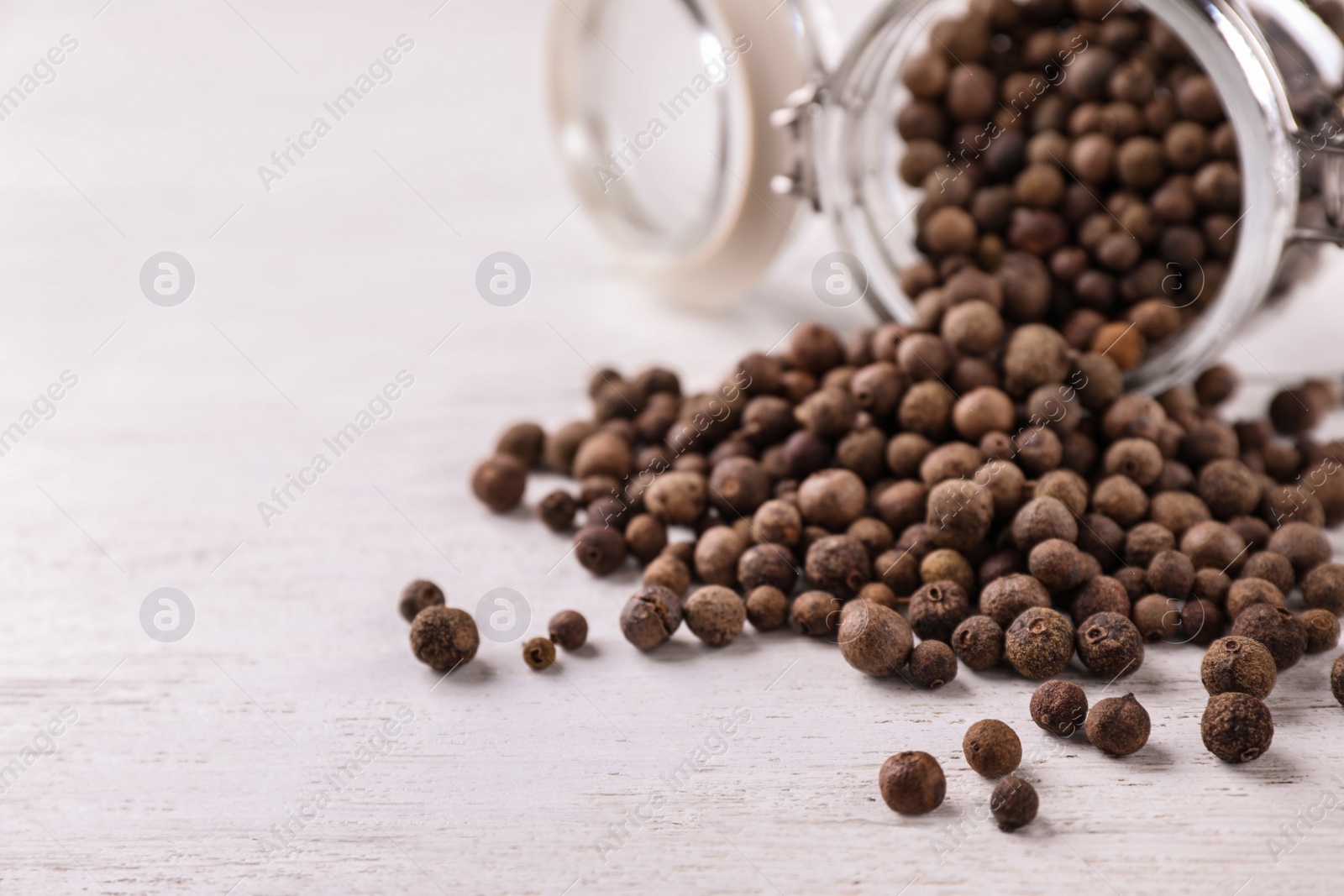 Photo of Black pepper grains on white wooden table, closeup